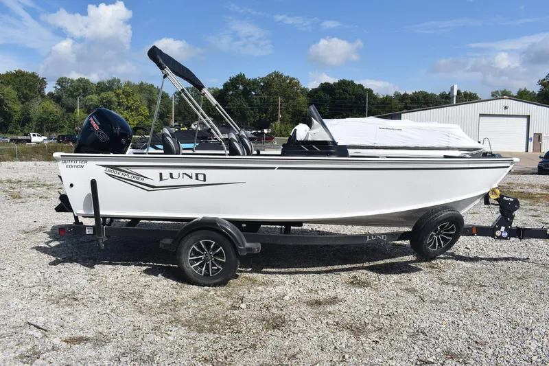 Slide: The Image of 2026 Lund 1800 Explorer SS boat with outboard motor, parked on gravel lot. - 5