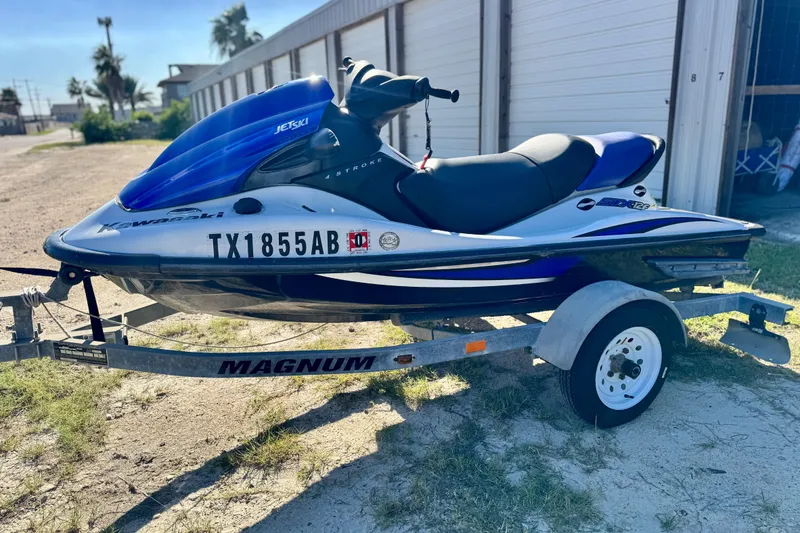 Slide: The Image of A blue Kawasaki Jet Ski on a trailer, parked outdoors near storage units. - 96