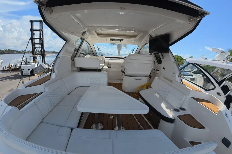 Slide: The Image of 2021 Sea Ray Sundancer 350 Coupe interior with seating, table, and helm, docked by the water. - 6