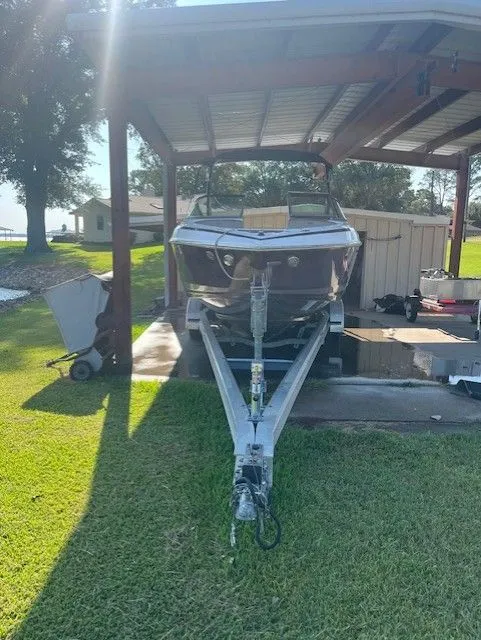 Slide: The Image of 2010 Regal 2500 boat on trailer under a metal canopy, parked on grass. - 2