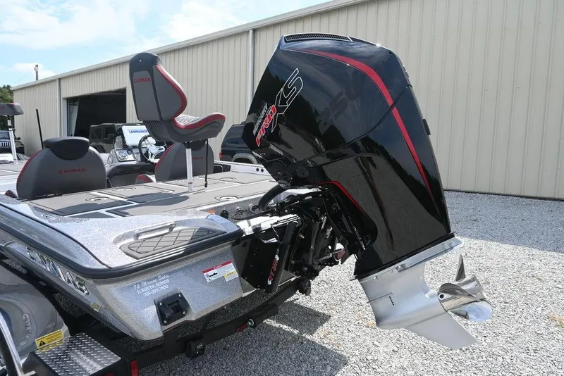 Slide: The Image of 2026 Caymas XS 21 boat with powerful outboard motor, parked on gravel near a building. - 10