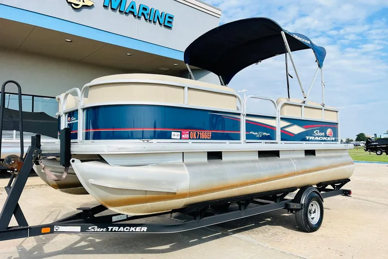 Slide: The Image of 2019 Sun Tracker Party Barge 18 DLX pontoon boat on trailer, parked outside marine store. - 2