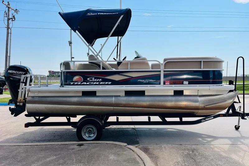Slide: The Image of 2019 Sun Tracker Party Barge 18 DLX pontoon boat on trailer, featuring a Mercury outboard motor. - 5