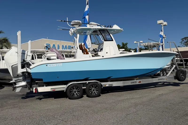 Slide: The Image of 2023 Costa Custom Boats 264 HC on trailer, displayed outdoors under clear blue sky. - 2