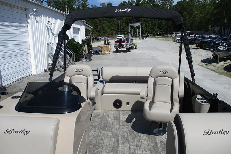 Slide: The Image of 2026 Bentley Pontoons 223 Legacy Swingback with beige seating and canopy, parked outdoors. - 9
