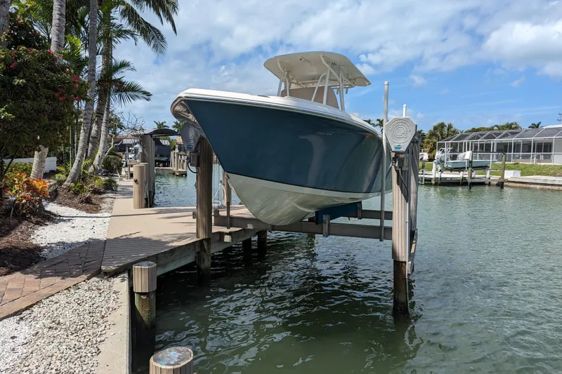 Slide: The Image of 2016 Sailfish 240 CC boat docked on lift by waterfront, surrounded by palm trees. - 3