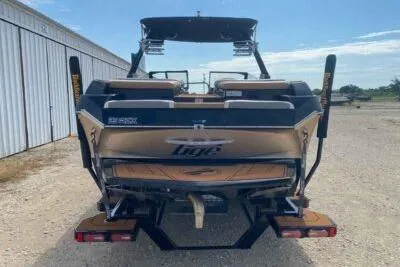 Slide: The Image of 2021 Tigé 23RZX boat, rear view, parked on gravel near a storage facility. - 5