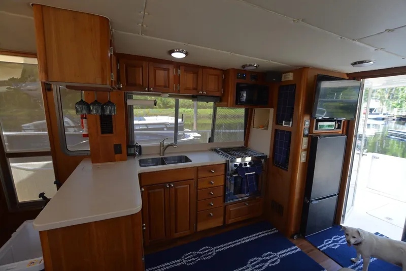 Slide: The Image of 2004 Mainship 400 Trawler kitchen interior with wood cabinetry, appliances, and a dog on a blue rug. - 16