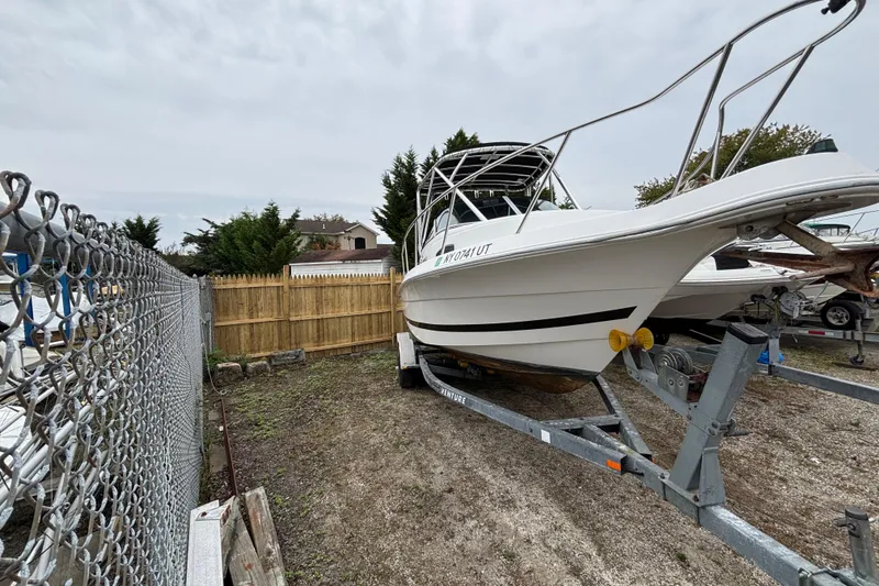 Slide: The Image of 1999 Wellcraft 22 Coastal Walkaround O/B boat on trailer, parked near chain-link fence. - 3