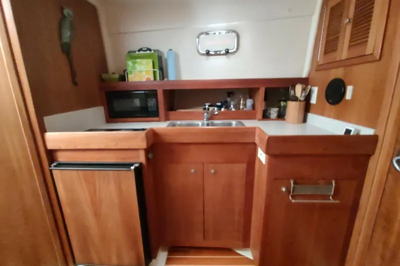 Slide: The Image of 2003 Mainship 34 PILOT boat kitchen with wooden cabinets, sink, and microwave. - 15