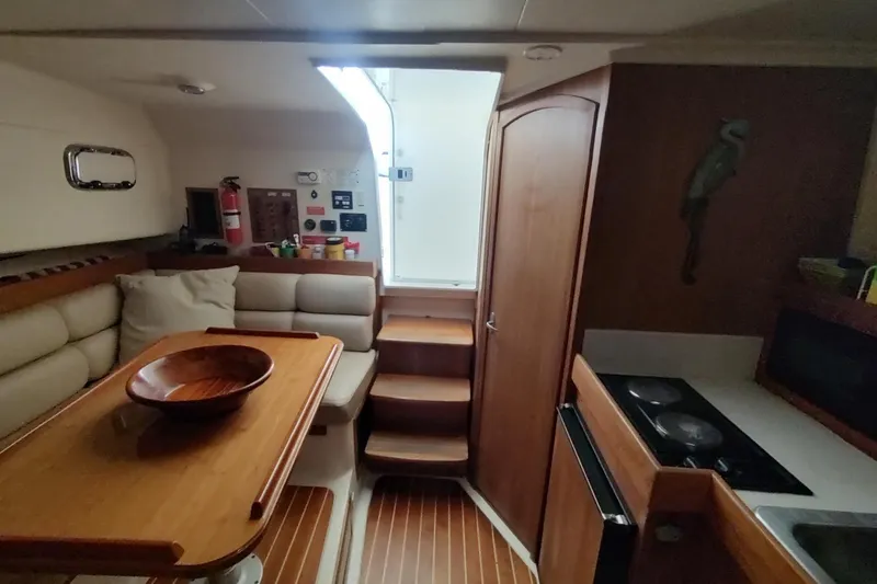 Slide: The Image of 2003 Mainship 34 PILOT interior with cozy seating, wooden table, and compact kitchen area. - 26