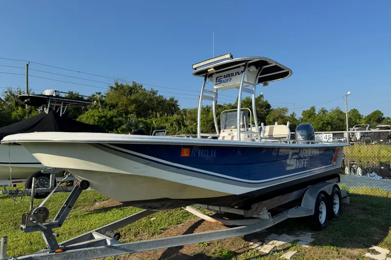 The Image of 2012 Carolina Skiff 238 DLV boat on trailer, parked outdoors under clear blue sky. - 1