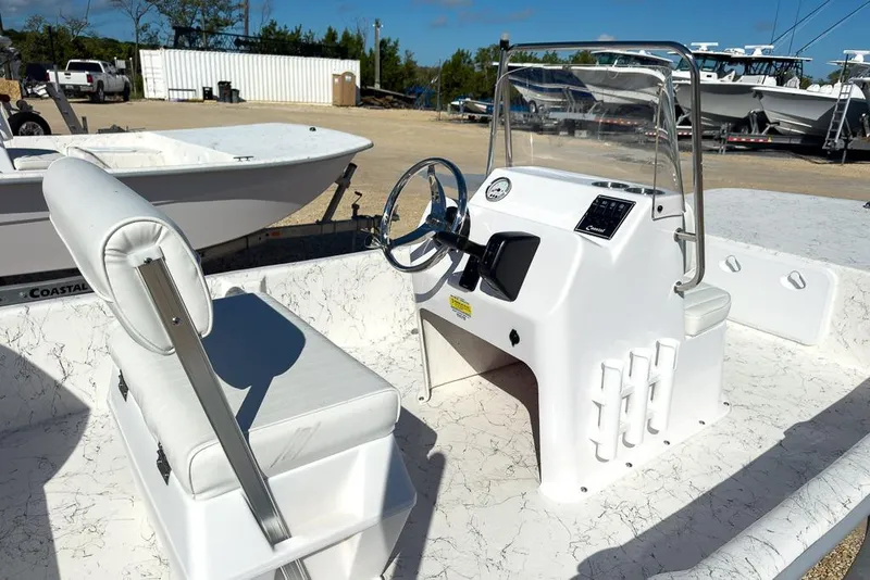 Slide: The Image of 2026 Coastal Skiff 171 boat interior with steering console and seating, parked outdoors. - 11