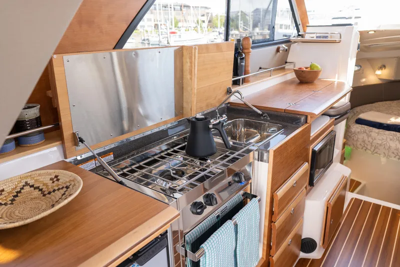 Slide: The Image of 2025 Cutwater C-32 Coupe yacht kitchen with stove, sink, and wooden cabinetry. - 8
