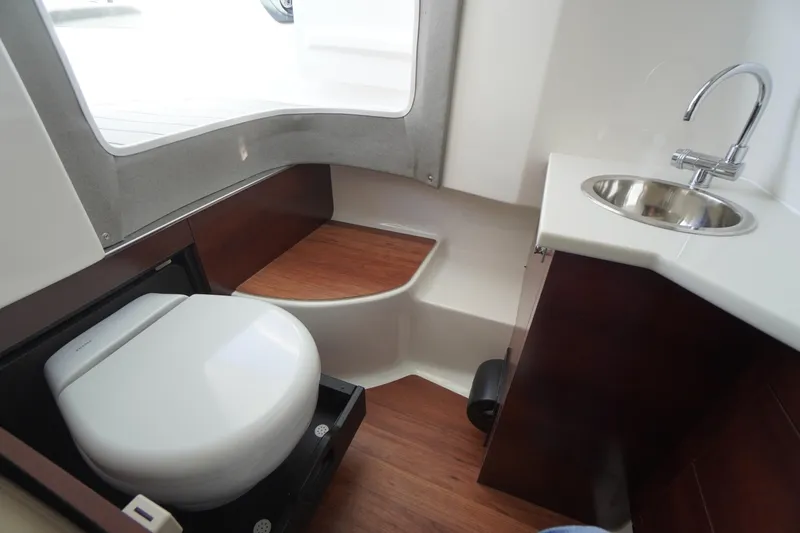 Slide: The Image of 2026 Chaparral 280 OSX boat interior with toilet and sink, featuring wood accents. - 22