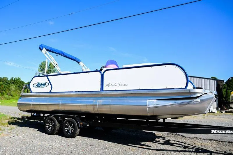 Slide: The Image of 2023 Aloha Pontoon boat on trailer under clear blue sky. - 2