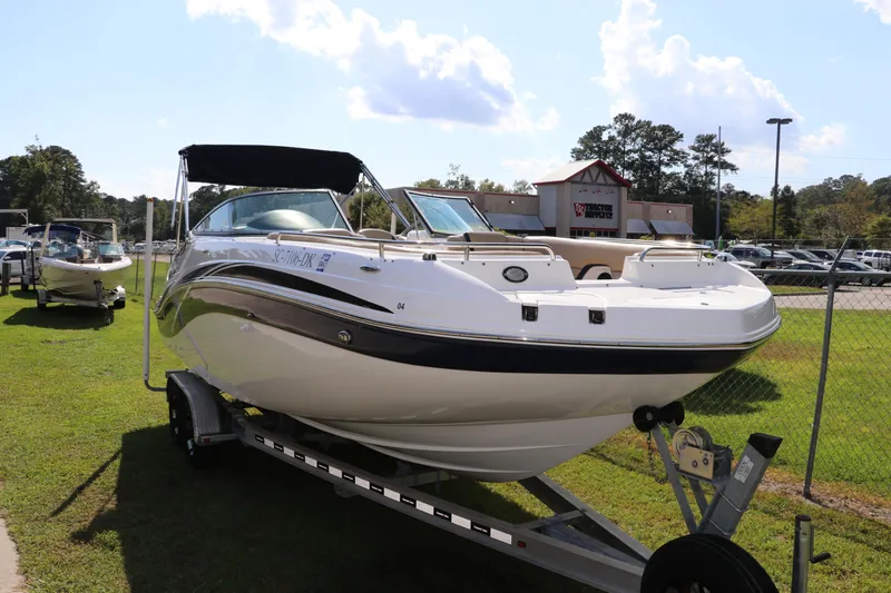 Slide: The Image of 2019 Hurricane SunDeck 2486 OB boat on trailer, parked on grass under a sunny sky. - 2