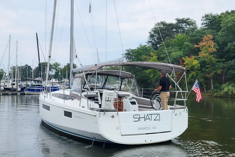Slide: The Image of 2022 Jeanneau Sun Odyssey 410 sailboat navigating a marina, with trees in the background. - 2