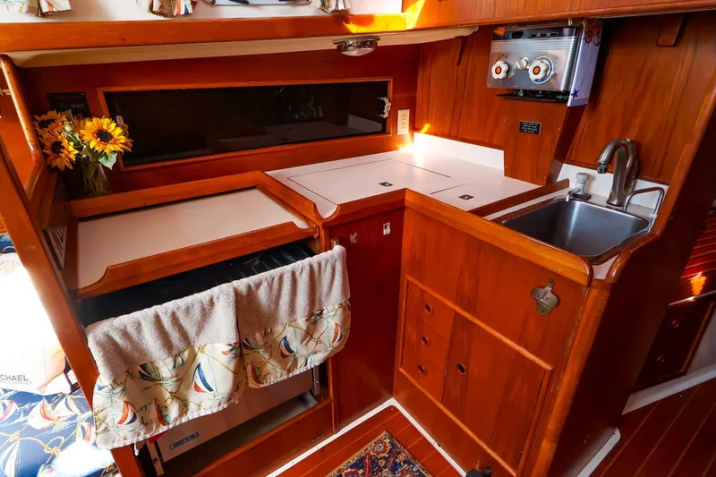 Slide: The Image of 1988 Nonsuch 30 Ultra yacht kitchen with wooden cabinetry, sink, and floral decor. - 13