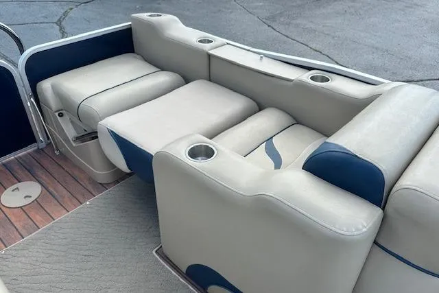 Slide: The Image of 2014 Manitou 24 Oasis SR boat interior with beige and blue seating, cup holders, and wood-style flooring. - 26