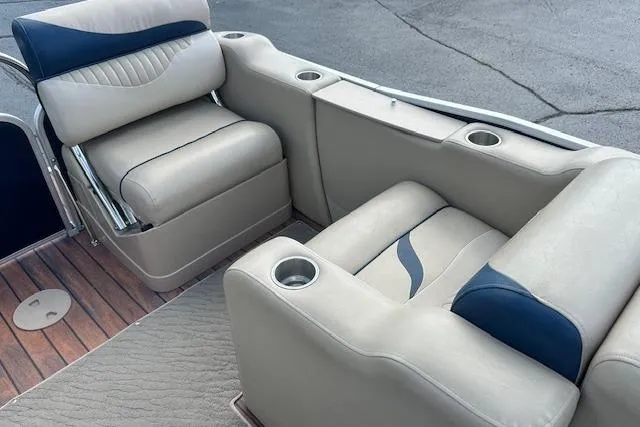 Slide: The Image of 2014 Manitou 24 Oasis SR boat interior with beige and blue seating, cup holders, and wood flooring. - 27