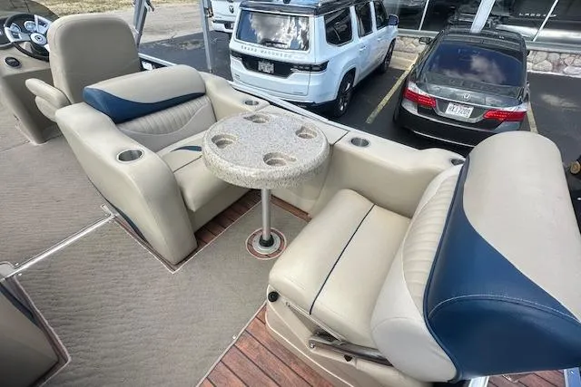 Slide: The Image of 2014 Manitou 24 Oasis SR boat interior with beige and blue seating, round table, and cup holders. - 8