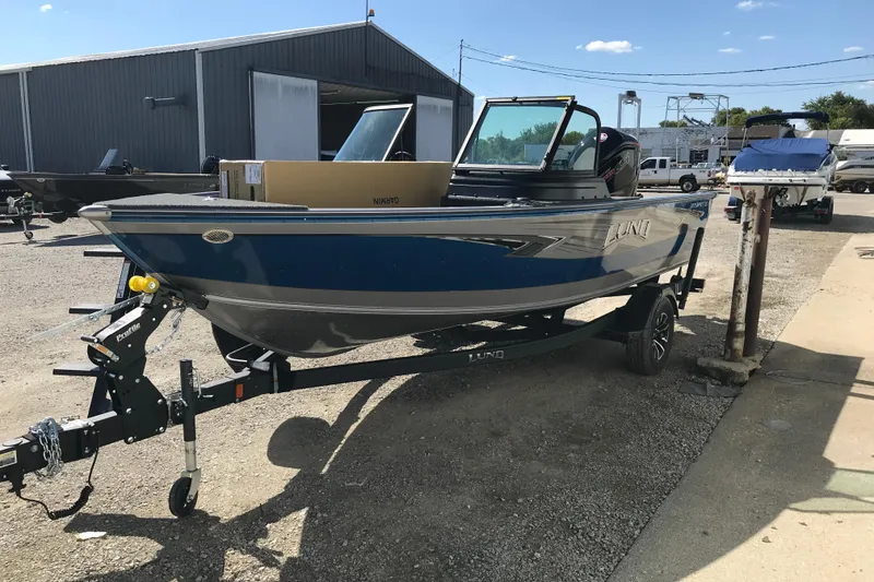 Slide: The Image of 2026 Lund 1875 Impact XS SS boat displayed indoors with vibrant blue exterior. - 1