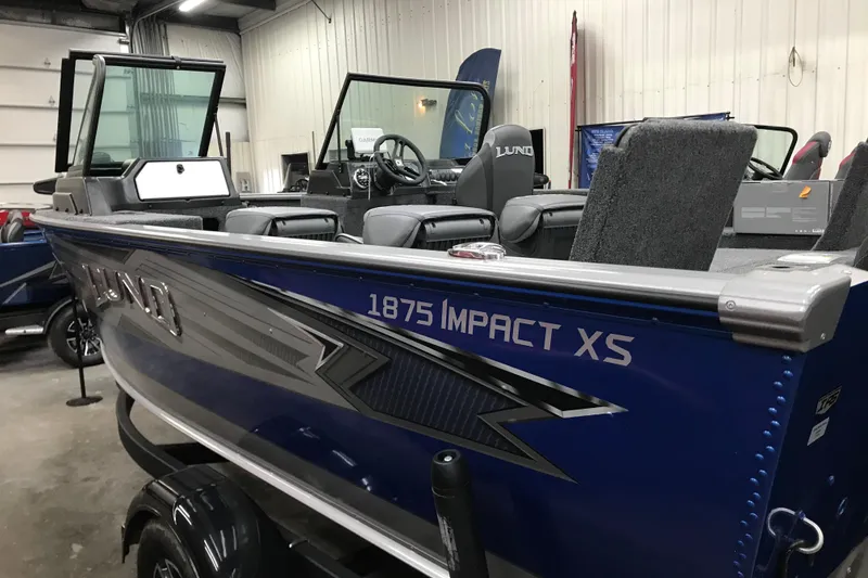 Slide: The Image of 2026 Lund 1875 Impact XS SS boat in showroom, featuring sleek design and modern interior. - 7