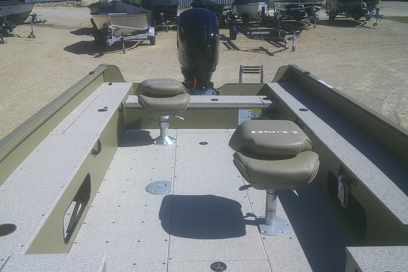 Slide: The Image of 2026 Lund 1875 Alaskan Tiller boat interior with seating and motor, parked on gravel. - 5