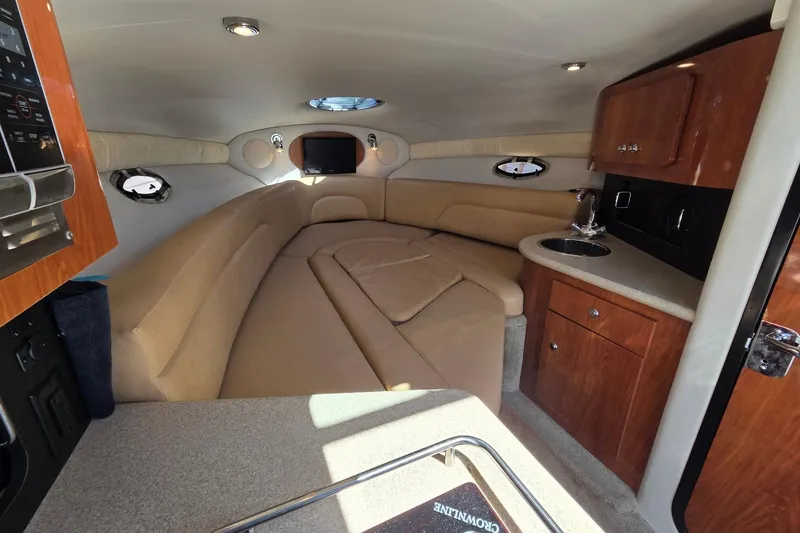 Slide: The Image of 2013 Crownline 325 SCR cabin interior with beige seating, kitchenette, and porthole windows. - 14