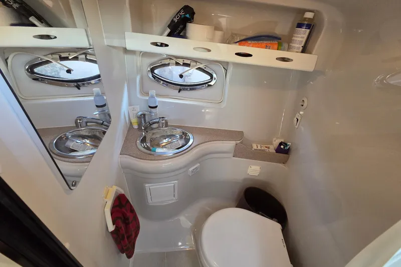 Slide: The Image of Compact bathroom in 2013 Crownline 325 SCR boat with sink, mirror, and storage shelves. - 18