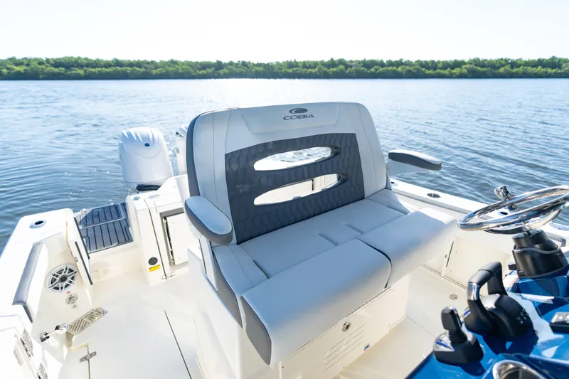 Slide: The Image of 2026 Cobia 245 Center Console boat interior with seating and steering wheel on calm water. - 11