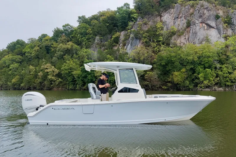 The Image of 2027 Cobia 245 Center Console boat on calm water near rocky, forested shoreline. - 0