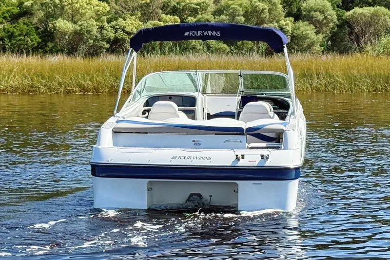 Slide: The Image of 2000 Four Winns 260 Horizon boat cruising on a calm lake with lush greenery. - 7