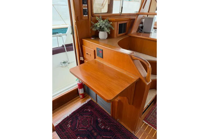 Slide: The Image of 1988 Offshore Yachts 48 Sedan interior with wooden desk, fire extinguisher, and decorative plant. - 55