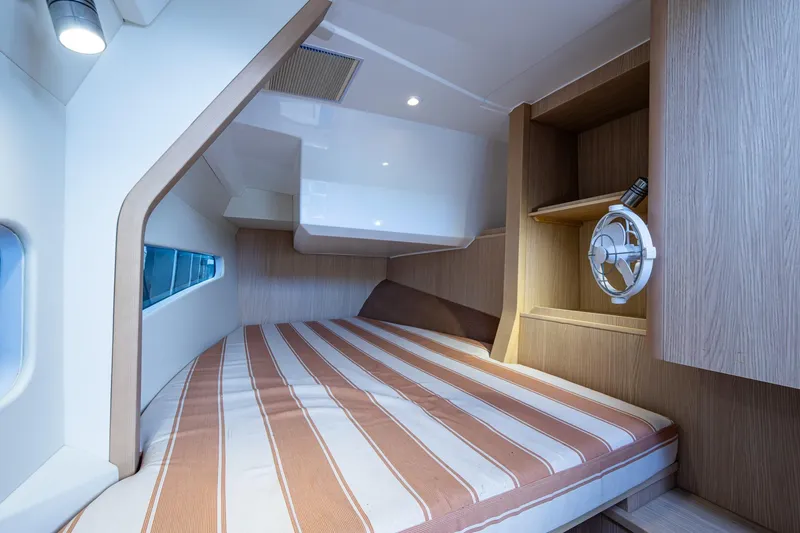 Slide: The Image of 2023 Aquila 32 Power Cat cabin with striped bedding and wooden interior design. - 2