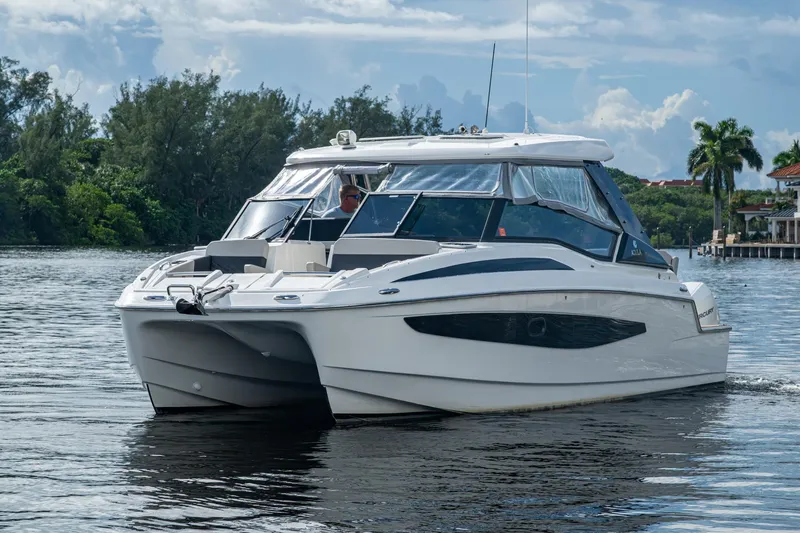 Slide: The Image of 2023 Aquila 32 Power Cat cruising on a serene waterway with lush greenery. - 36
