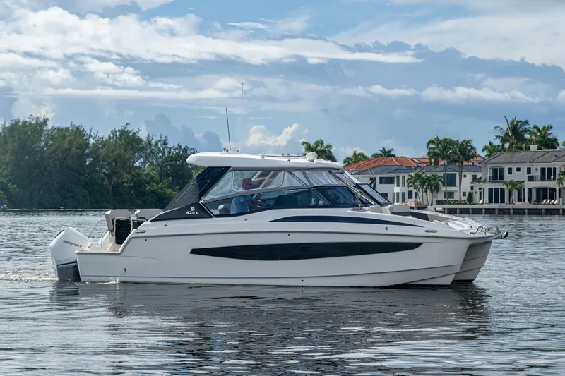 Slide: The Image of 2023 Aquila 32 Power Cat cruising on a scenic waterfront with luxury homes. - 42