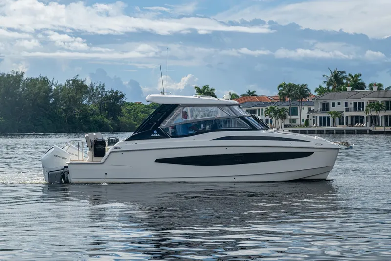 Slide: The Image of 2023 Aquila 32 Power Cat cruising on a scenic waterfront with luxury homes. - 43