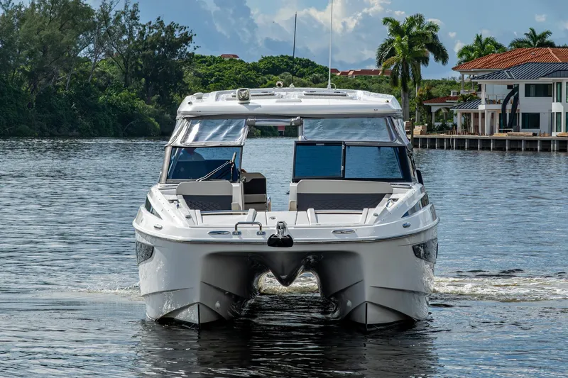 Slide: The Image of 2023 Aquila 32 Power Cat cruising on a scenic waterway near luxury homes. - 53