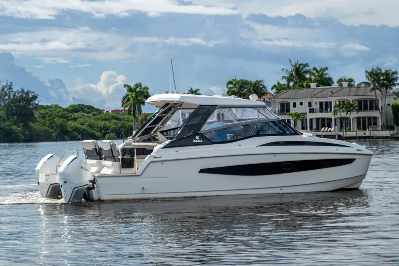 Slide: The Image of Aquila 32 Power Cat 2023 cruising on a scenic waterway with luxury homes in the background. - 55