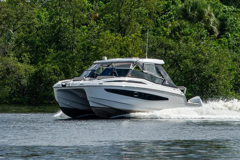 Slide: The Image of 2023 Aquila 32 Power Cat cruising on a scenic waterway with lush greenery. - 58