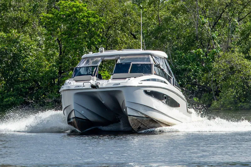 Slide: The Image of 2023 Aquila 32 Power Cat cruising on a serene waterway surrounded by lush greenery. - 59
