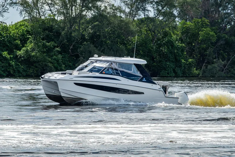 Slide: The Image of 2023 Aquila 32 Power Cat cruising on a river with lush greenery in the background. - 72