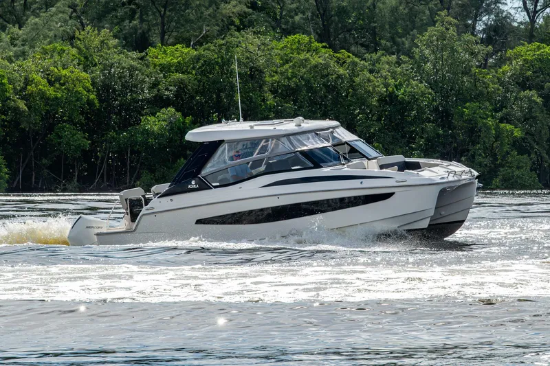 Slide: The Image of 2023 Aquila 32 Power Cat cruising on a river with lush green trees in the background. - 76