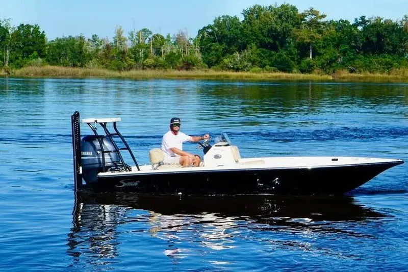 The Image of 2023 Scout 177 Sport boat on calm water with lush green shoreline. - 0