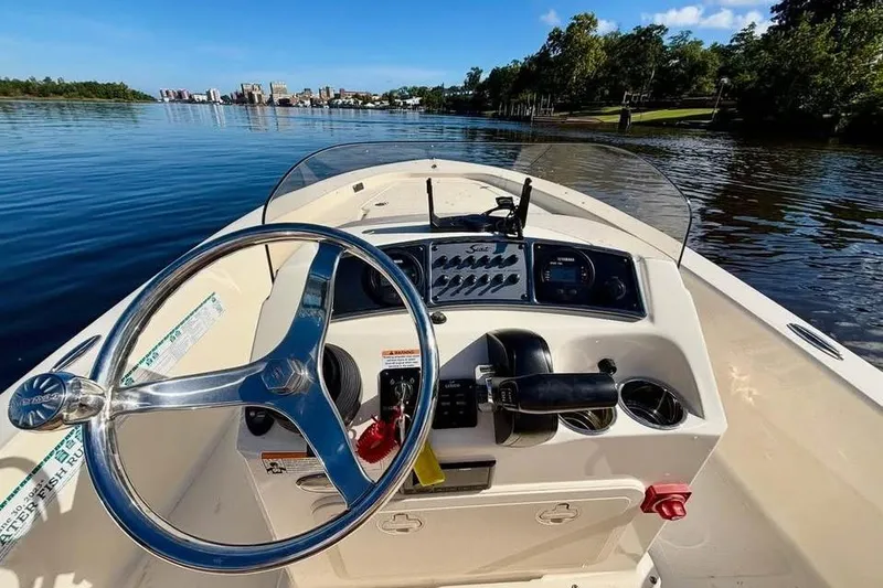 Slide: The Image of 2023 Scout 177 Sport boat dashboard with steering wheel on a calm lake. - 8