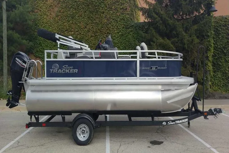 The Image of 2026 Sun Tracker Bass Buggy 16 XL Select pontoon boat on trailer, parked outdoors. - 0