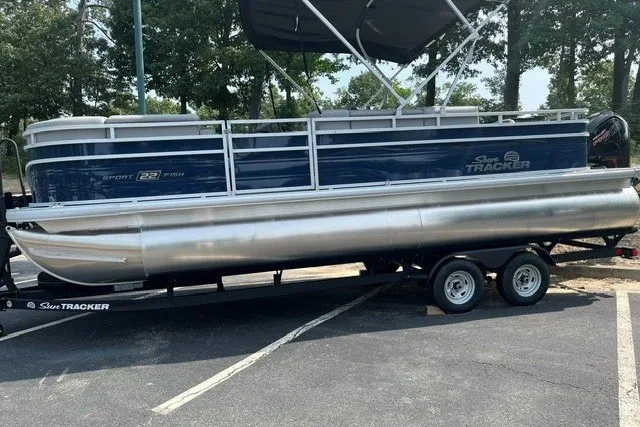 The Image of 2026 Sun Tracker SportFish 22 DLX pontoon boat on trailer in parking lot. - 0