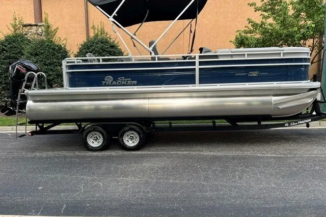 The Image of 2026 Sun Tracker SportFish 22 DLX pontoon boat on trailer, parked outdoors. - 0